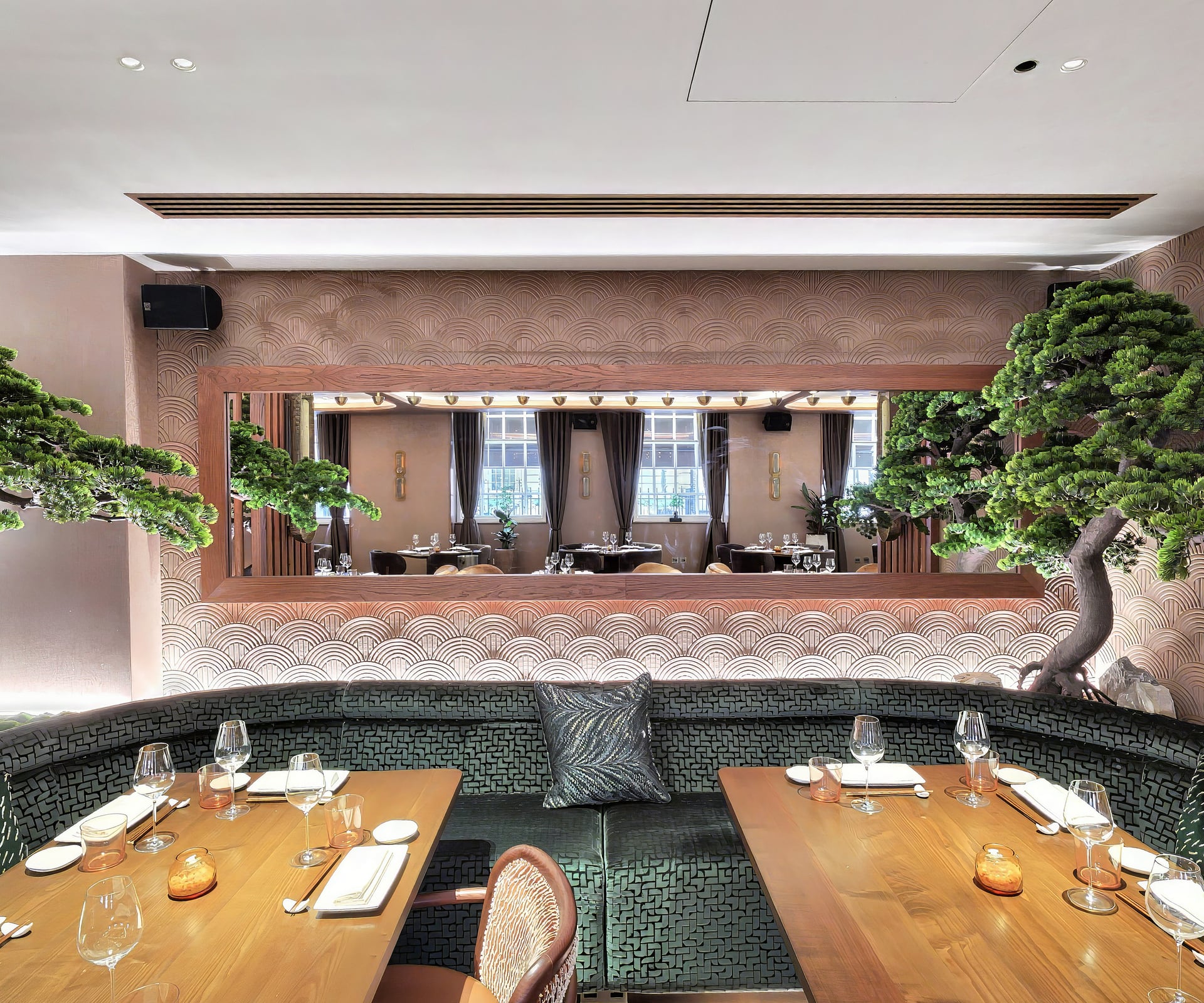 A private dining booth at MA/NA Mayfair with a bonsai, mirror-backed banquette and a set walnut table