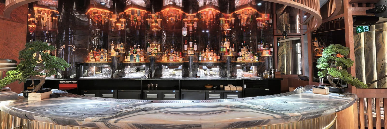 The sweeping marble bar at MA/NA, its back bar glowing beneath the slatted timber canopy