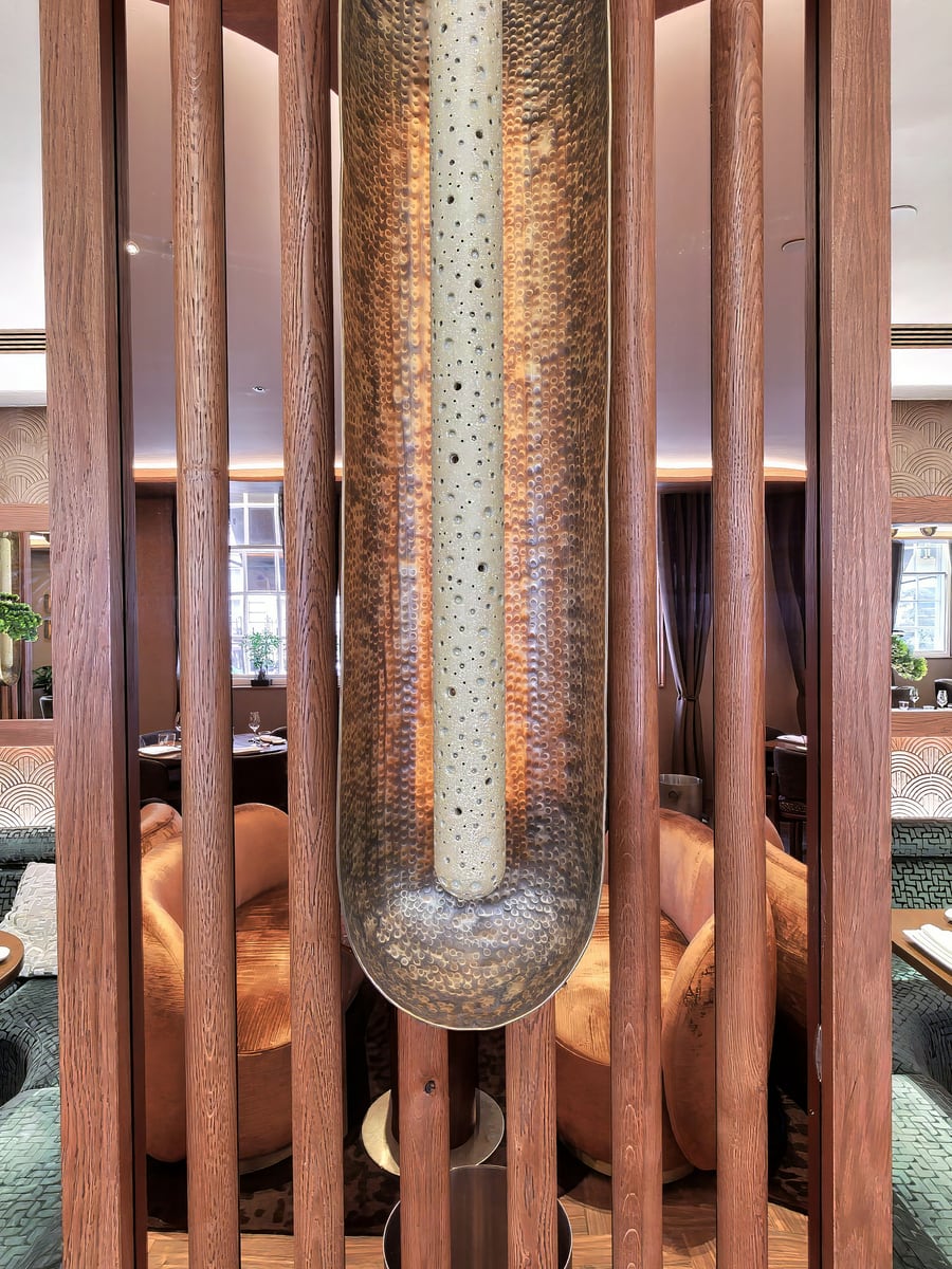 A hammered metal column lit from within, framed by timber battens between the dining booths