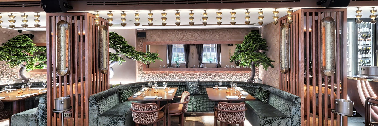 The dining room beneath its run of brass pendants, with bonsai between the booths